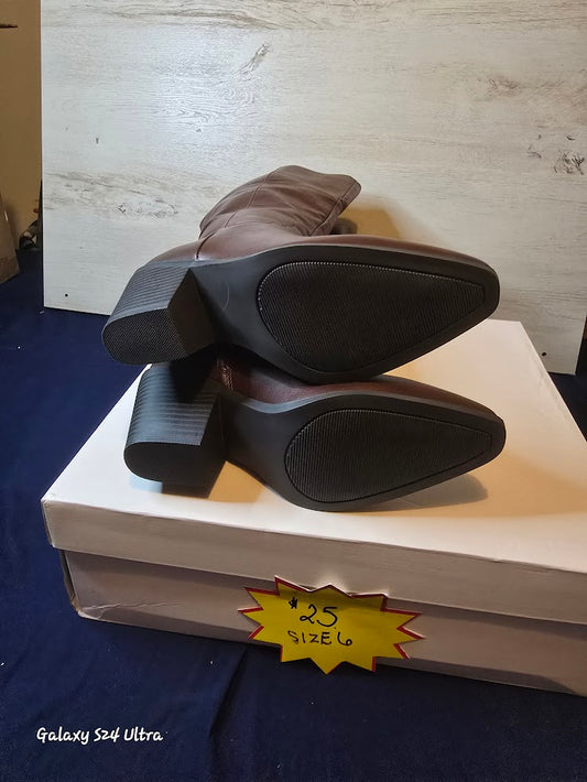 Brown boots on a white box with a price tag in front of a wooden panel.