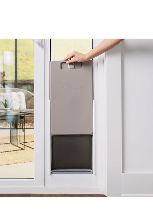 Person opening a pet door in a glass door with a view of a living room.
