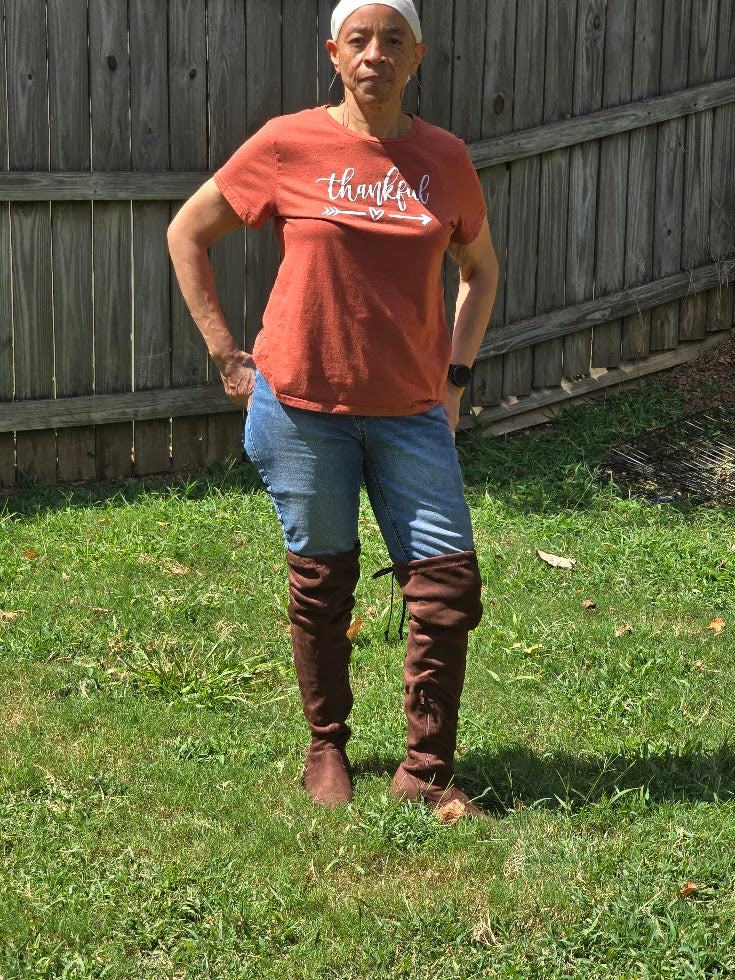 Person wearing a 'thankful' t-shirt and chocolate brown over the knee boots standing on grass.