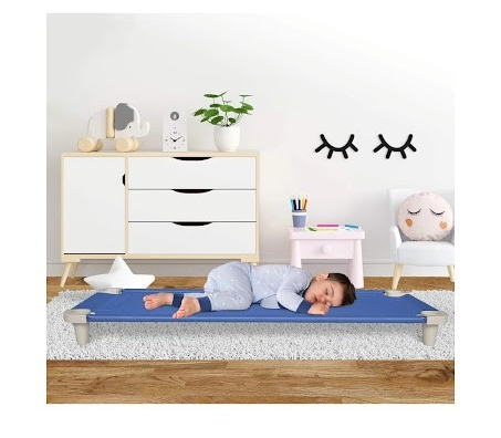 Child lying on a blue nap cot in a room with a white dresser and decorative items.