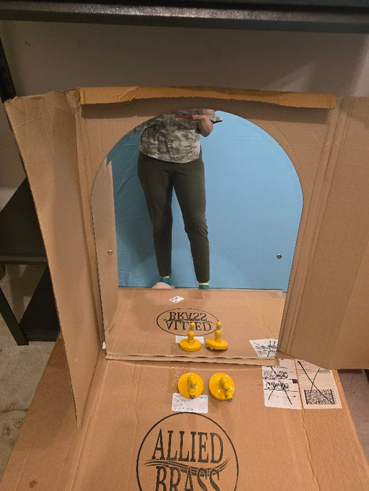 Person taking a mirror selfie inside a cardboard box with 'Allied Brass' branding