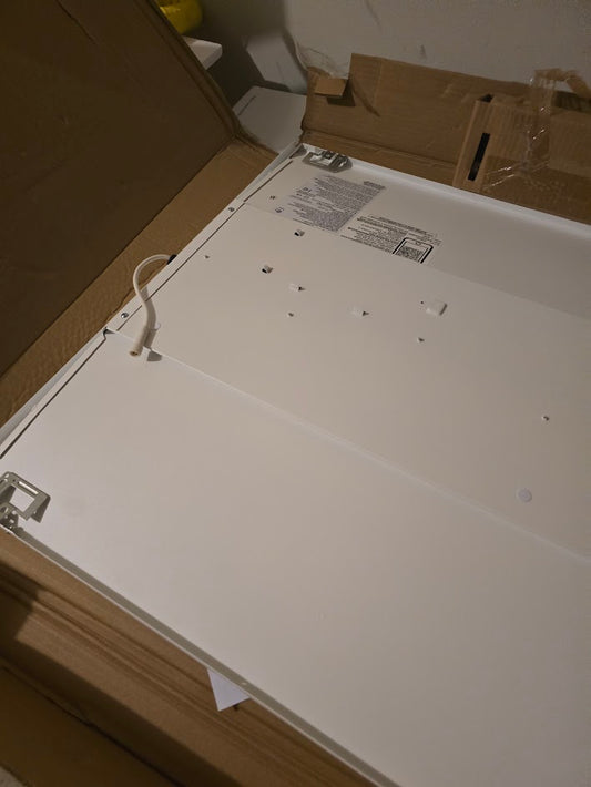 Back of a white troffer light with mounting holes showing, displayed on a cardboard box