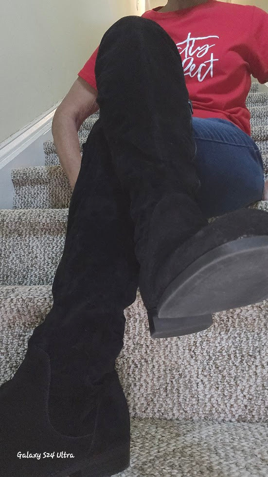 Person wearing black boots sitting on a carpeted staircase