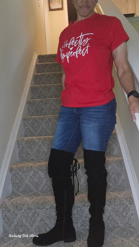 Person wearing a red t-shirt with text, blue jeans, and black knee-high boots standing on a staircase.