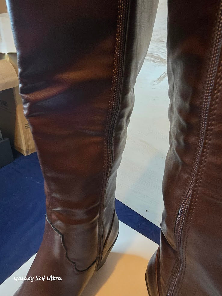 Brown leather knee-high boots on a person standing on a blue and white floor.