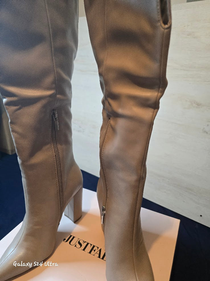  Close up tan knee-high boots on a mannequin with 'JUSTFAB' branding